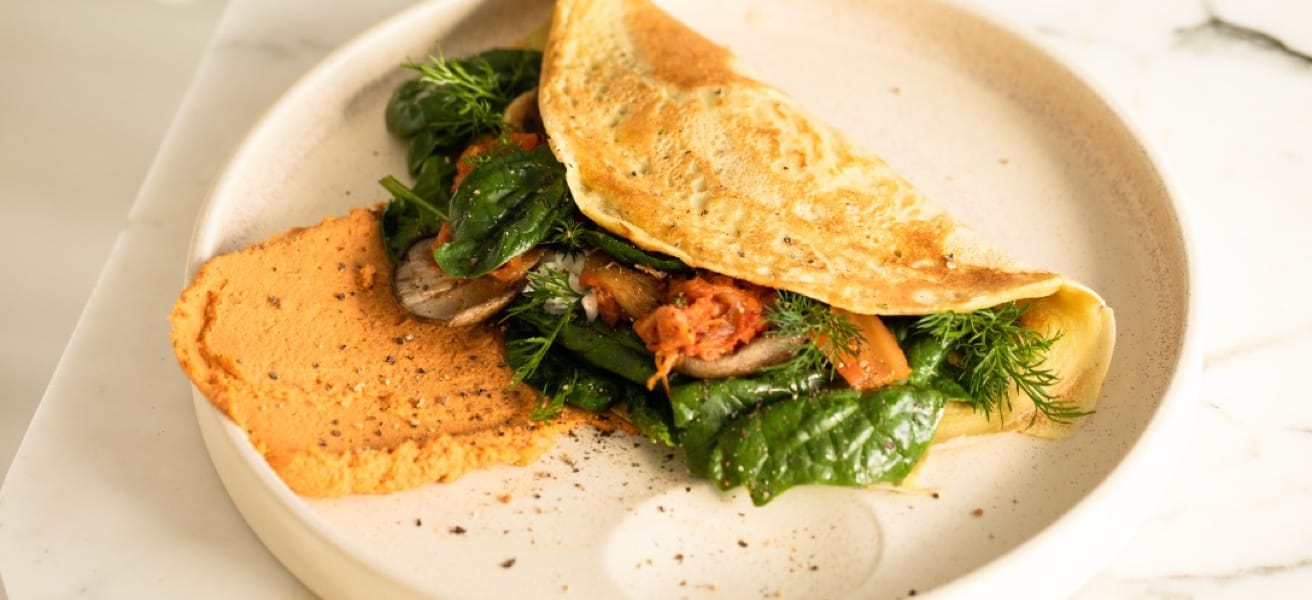  A colorful omelette filled with spinach and hummus sits on a white plate